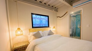 Une chambre à coucher avec un lit, un téléviseur fixé au mur et une porte de douche en verre.