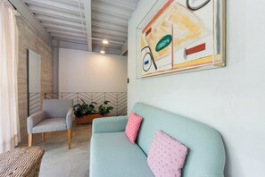 Een kamer met een lichtblauwe bank, een grijze fauteuil en een rieten tafeltje.
