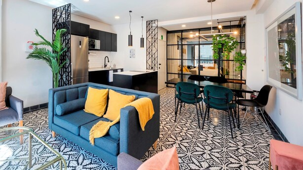 Een moderne zithoek met een bank, stoelen, een eettafel en een keuken op de achtergrond.
