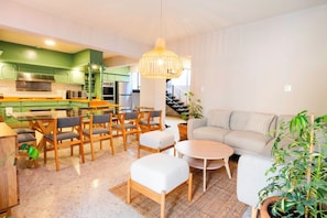 A modern kitchen with green cabinets, a dining area with wooden chairs and a table, a sofa, and a hanging light fixture. - COMPLEJO MATAMOROS · Oasis Urbano con Piscina y Gimnasio (Oaxaca)