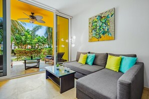 A modern living room with a grey sofa, colorful cushions, a glass coffee table, and a painting on the wall. - Cozy 1BR/1BA Isla Bonita Getaway Pool&BBQ (Noord)