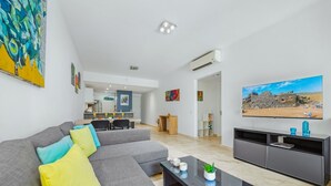 Een moderne woonkamer met een hoekbank, een flatscreen televisie en een eethoek op de achtergrond.