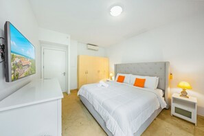 A hotel room with a bed, a desk, a television, and a wardrobe. - Cozy 1BR/1BA Isla Bonita Getaway Pool&BBQ (Noord)