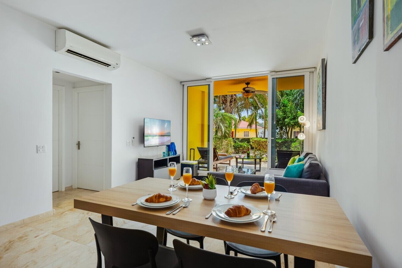 A dining area with a table set for breakfast, a TV mounted on the wall, and a view of the outdoors.