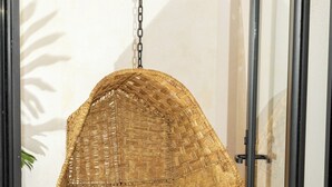 Una silla colgante de mimbre con cojín, una planta en maceta y un suelo de baldosas.