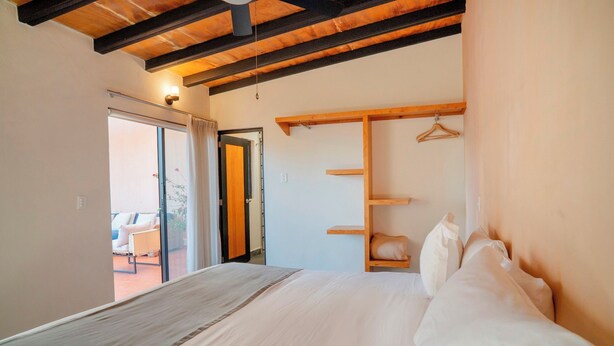 Une chambre à coucher comprenant un lit, une tête de lit en bois, un portant à vêtements et une porte coulissante donnant sur un balcon.