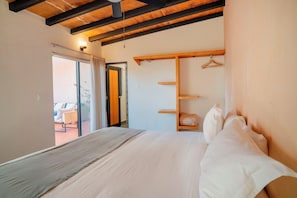 A bedroom with a bed, a wooden headboard, a hanging clothes rack, and a sliding door leading to a balcony.