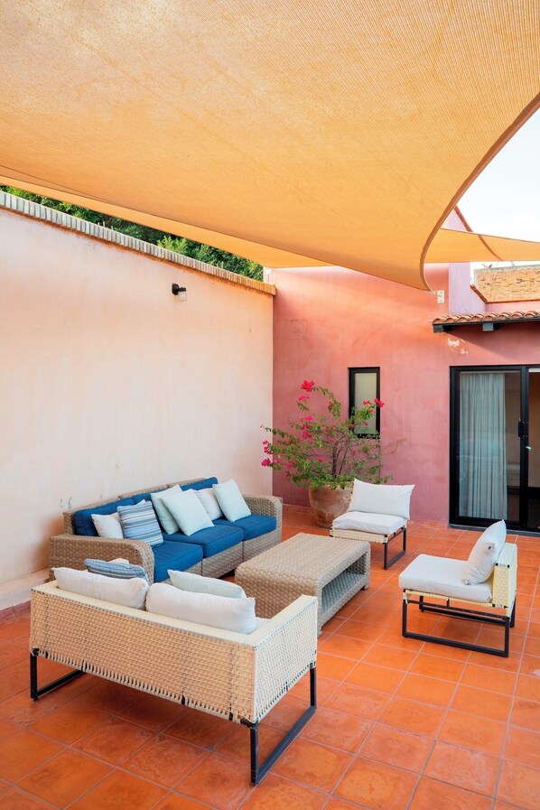 A covered outdoor seating area with wicker furniture, a potted plant, and a sliding glass door.