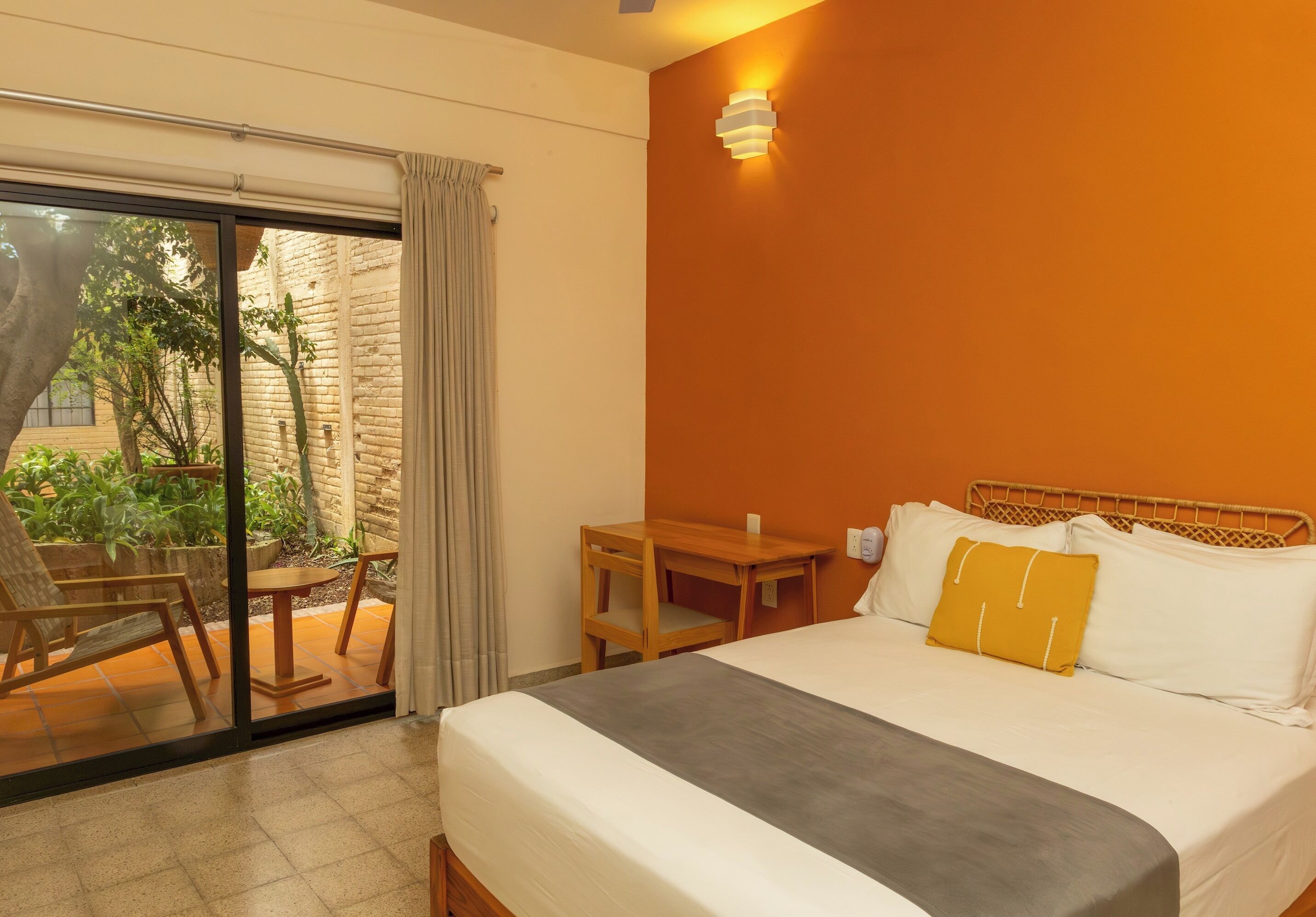 A hotel room with a bed, a small table, a chair, and a view of the outside.