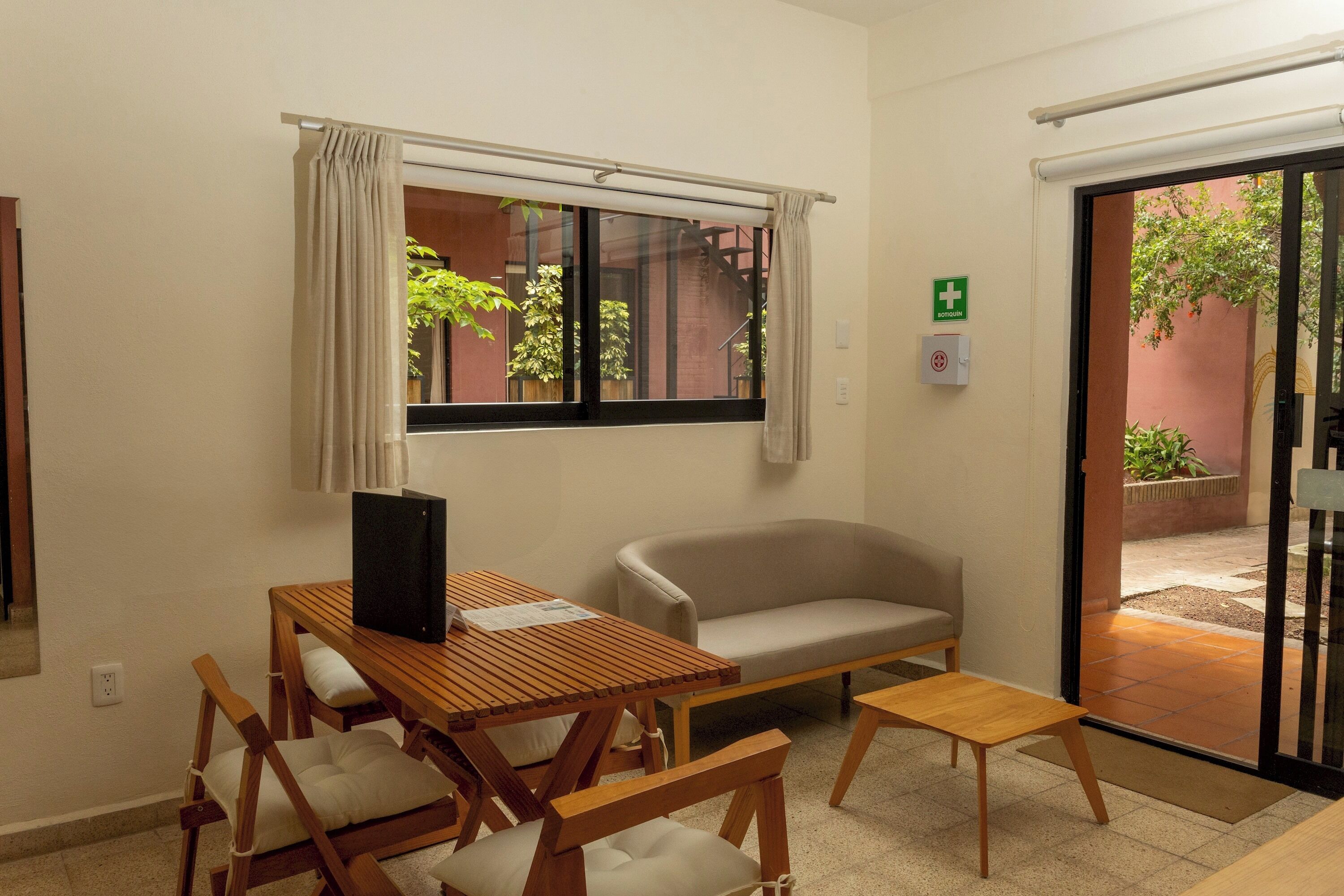 A room with a wooden table, two chairs, a sofa, a window with curtains, and a door leading outside.