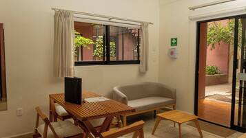 A room with a wooden table, two chairs, a sofa, a window with curtains, and a door leading outside.