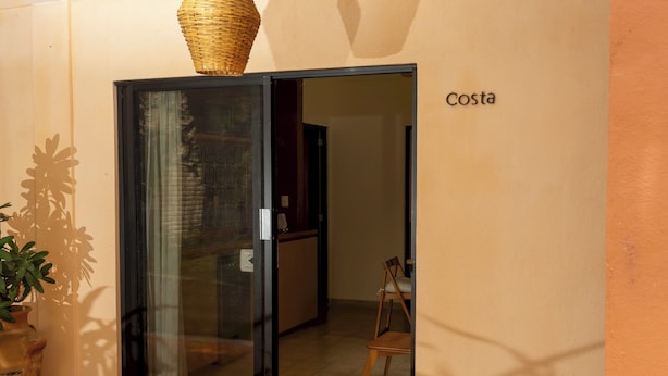 Ein Zimmer mit einer Schiebetür aus Glas, einem Korbwäscher an der Tür, einer Topfpflanze und einem Schild mit der Aufschrift 'Costa'.