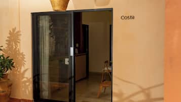 A room with a sliding glass door, a wicker basket on the door, a potted plant, and a sign that reads 'Costa'.