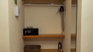 Un couloir étroit au sol carrelé de dalles rouges, une étagère en bois avec un coussin, un petit appareil noir et un miroir sur le mur de droite.