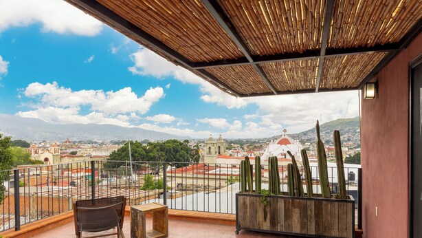 Un balcon donnant sur un paysage urbain, une chaise en bois et un pot contenant des cactus.