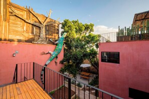 Une cour avec un bâtiment en bois, un mur rose, une sculpture verte et une terrasse en bois.