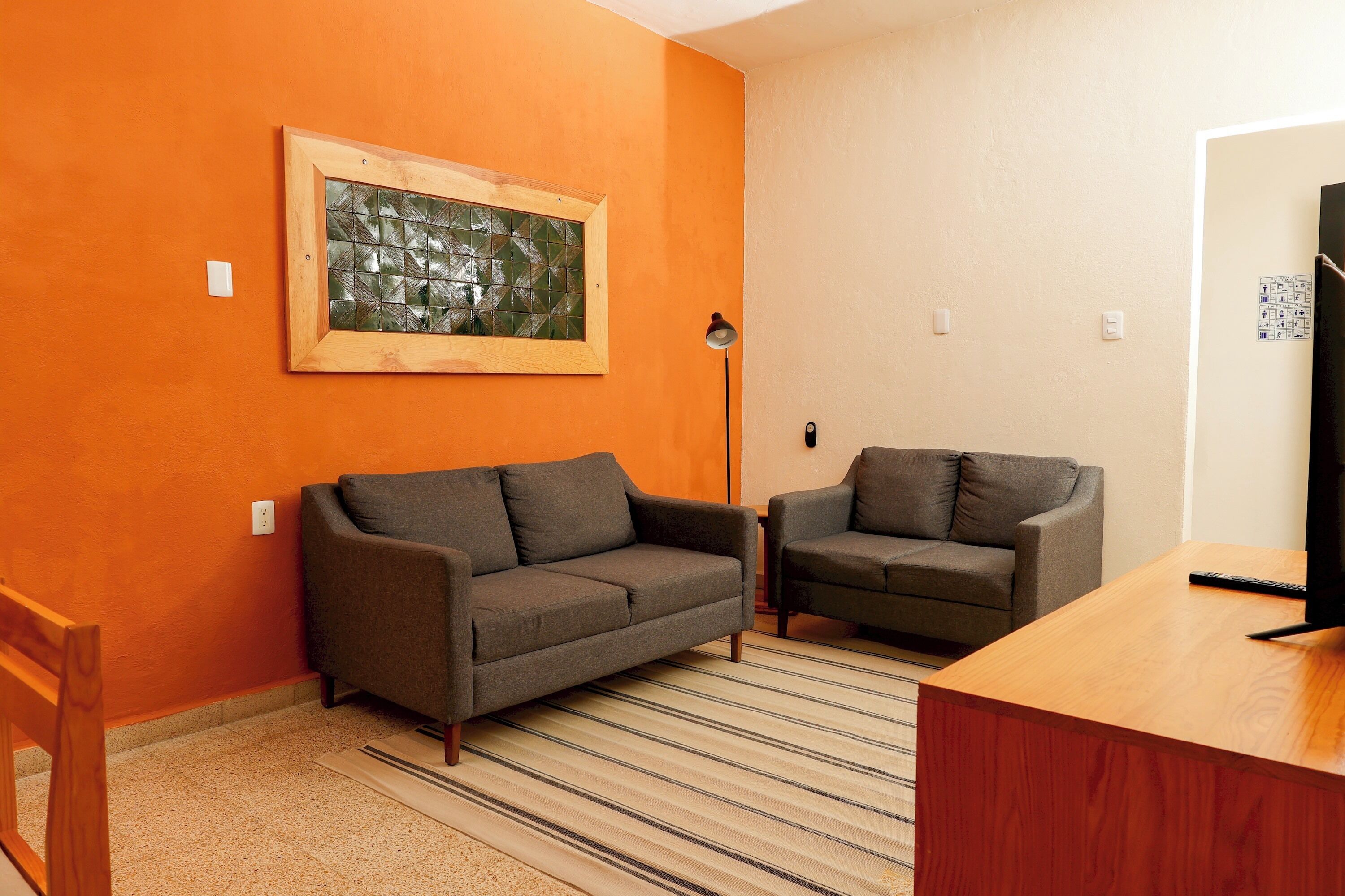 A room with two sofas, a wooden desk, a framed artwork on the wall, and a striped rug.