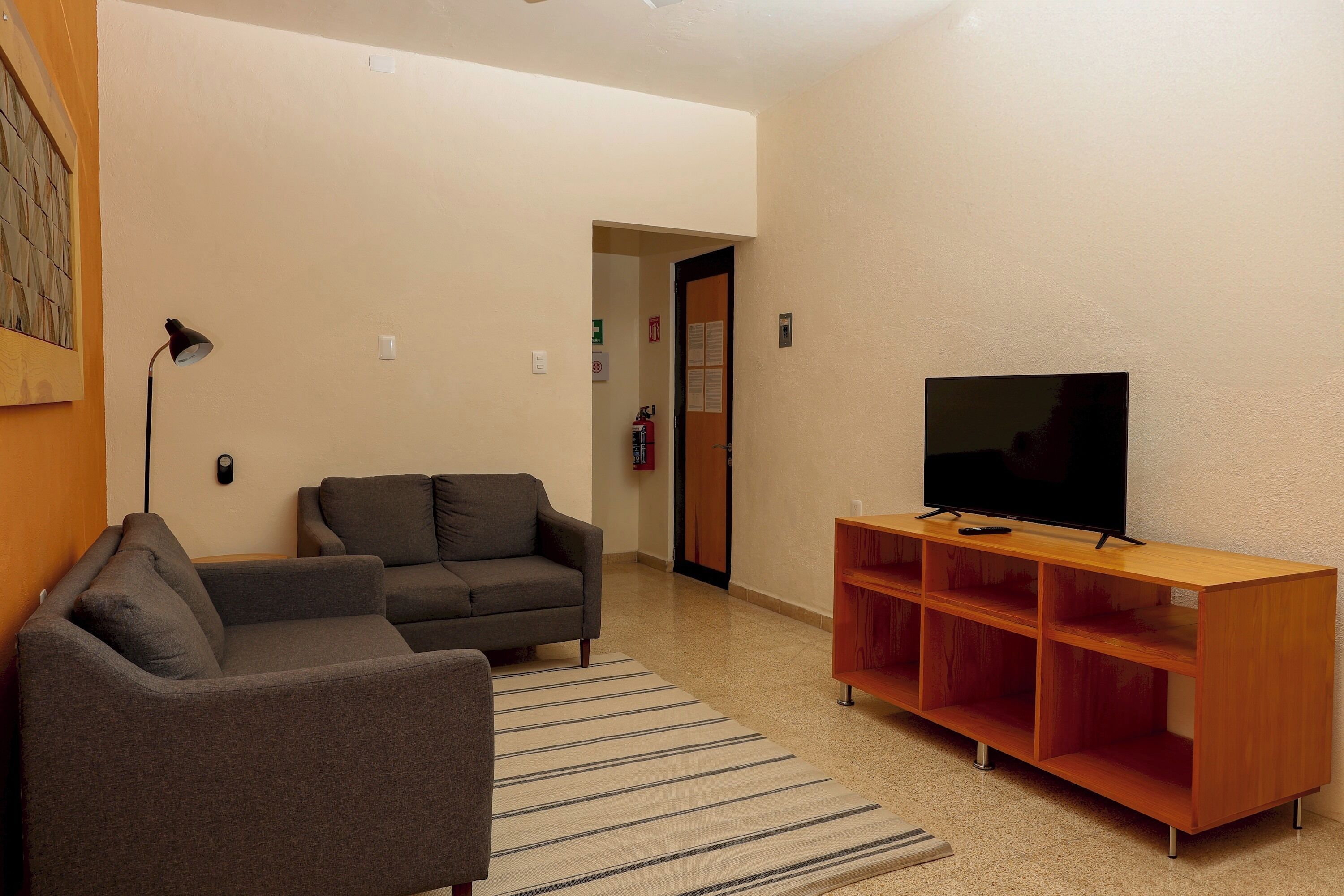 A living room with two sofas, a TV on a wooden stand, a striped rug, and a door leading to another room.