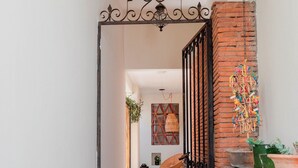 A hallway with a black metal gate, a brick wall, and a hanging decorative item. - HIDALGO 3 · Group Stay 2 Blocks from Zócalo (Oaxaca)