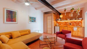 A modern living room with a sofa, armchairs, a glass coffee table, and a kitchen area with wooden cabinets and hanging plants. - HIDALGO 3 · Group Stay 2 Blocks from Zócalo (Oaxaca)