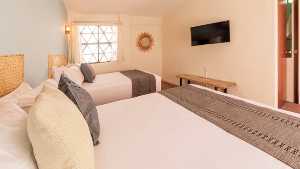 A bedroom with two beds, a TV, a window, and a sun-shaped wall decoration. - HIDALGO 3 · Group Stay 2 Blocks from Zócalo (Oaxaca)