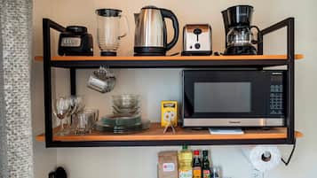 Une étagère de cuisine avec une machine à café, une bouilloire, un grille-pain et un four à micro-ondes.