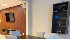 Ein moderner Essbereich mit einem dunklen Holztisch, weißen Polsterstühlen, einem an der Wand montierten Fernseher und einer eingebauten Vitrine mit Dekoration.