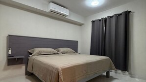 Ein Schlafzimmer mit Bett, Klimaanlage, Nachttisch und Vorhang.