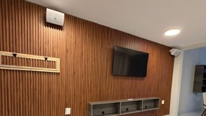 Ein modernes Wohnzimmer mit Holzpaneelen, einem montierten Fernseher, eingebauten Regalen, einem gelben Pouf und einem Marmorboden.