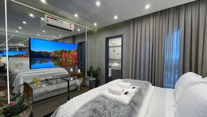 A modern hotel room with a large bed, a flat-screen TV, a mirror, and an air conditioning unit. - Paris Luxury Apartment (Barueri)