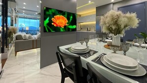 A modern dining area with a large flat-screen TV, a dining table set with plates and glasses, and a decorative vase with dried flowers. - Paris Luxury Apartment (Barueri)