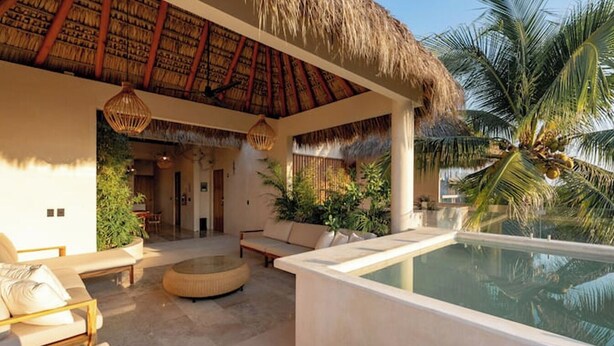 Un espace aménagé au bord de la piscine, doté d’un toit de chaume, de chaises longues et d’un petit coin salon.