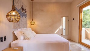 Une chambre à coucher avec un lit, deux lampes suspendues, une tapisserie murale, un miroir et une vue sur la verdure à l’extérieur.