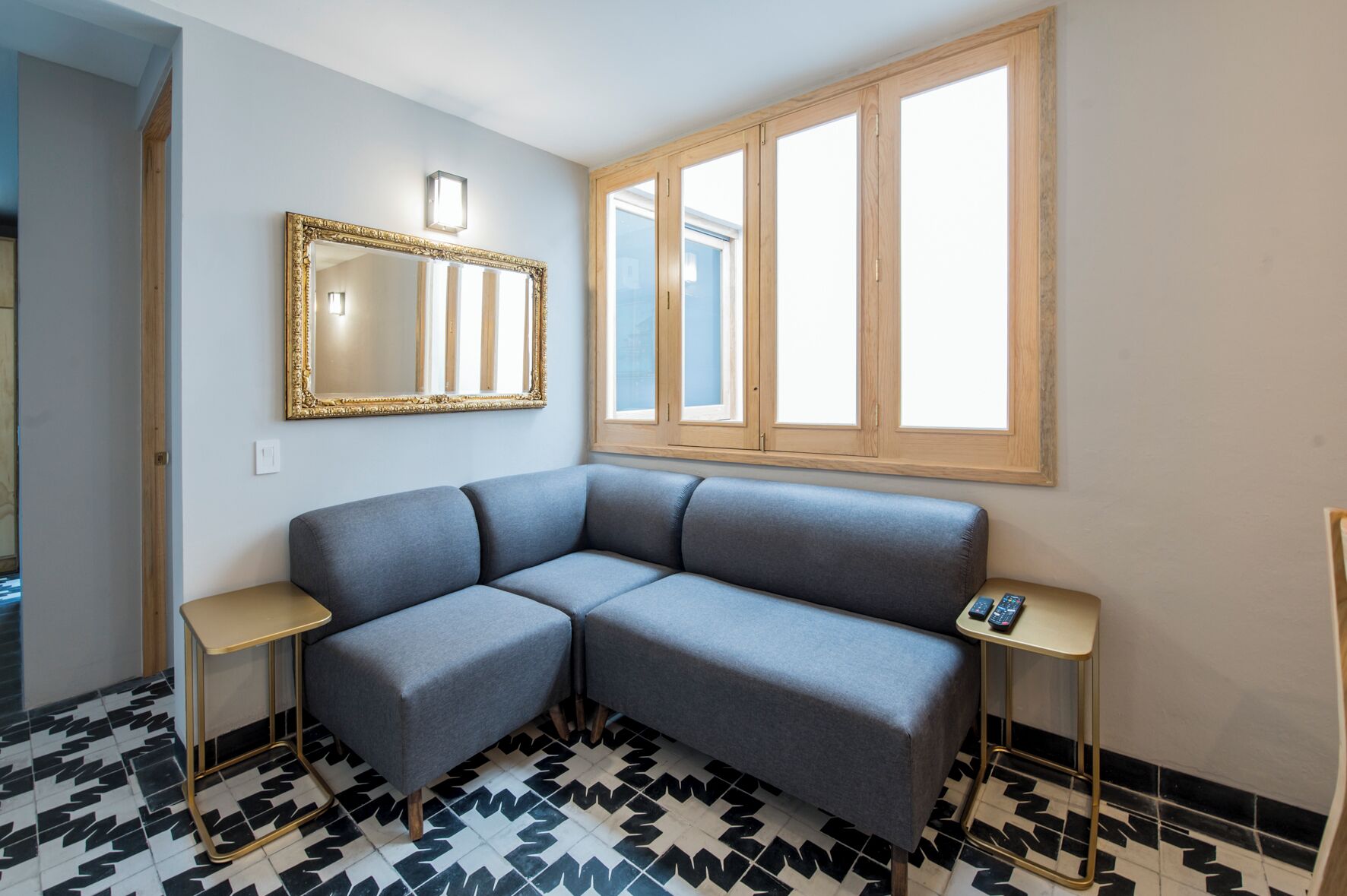A room with a gray sofa, a large mirror, two small tables, and a window with wooden frames.