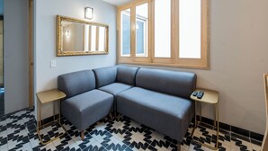 A room with a gray sofa, a large mirror, two small tables, and a window with wooden frames.