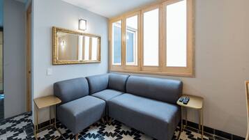 A room with a gray sofa, a large mirror, two small tables, and a window with wooden frames.