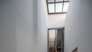 A narrow stairway with wooden steps and metal railings, leading to a landing with a skylight.