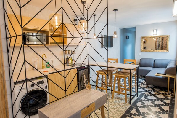 A compact living space with a kitchen, dining area, and seating area, featuring a geometric wall design and modern furnishings.