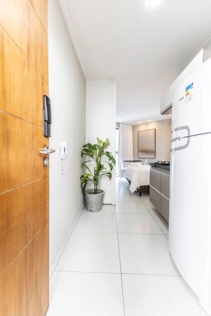 A narrow hallway with a wooden door, a potted plant, a telephone, and a kitchen area with a refrigerator and stove.