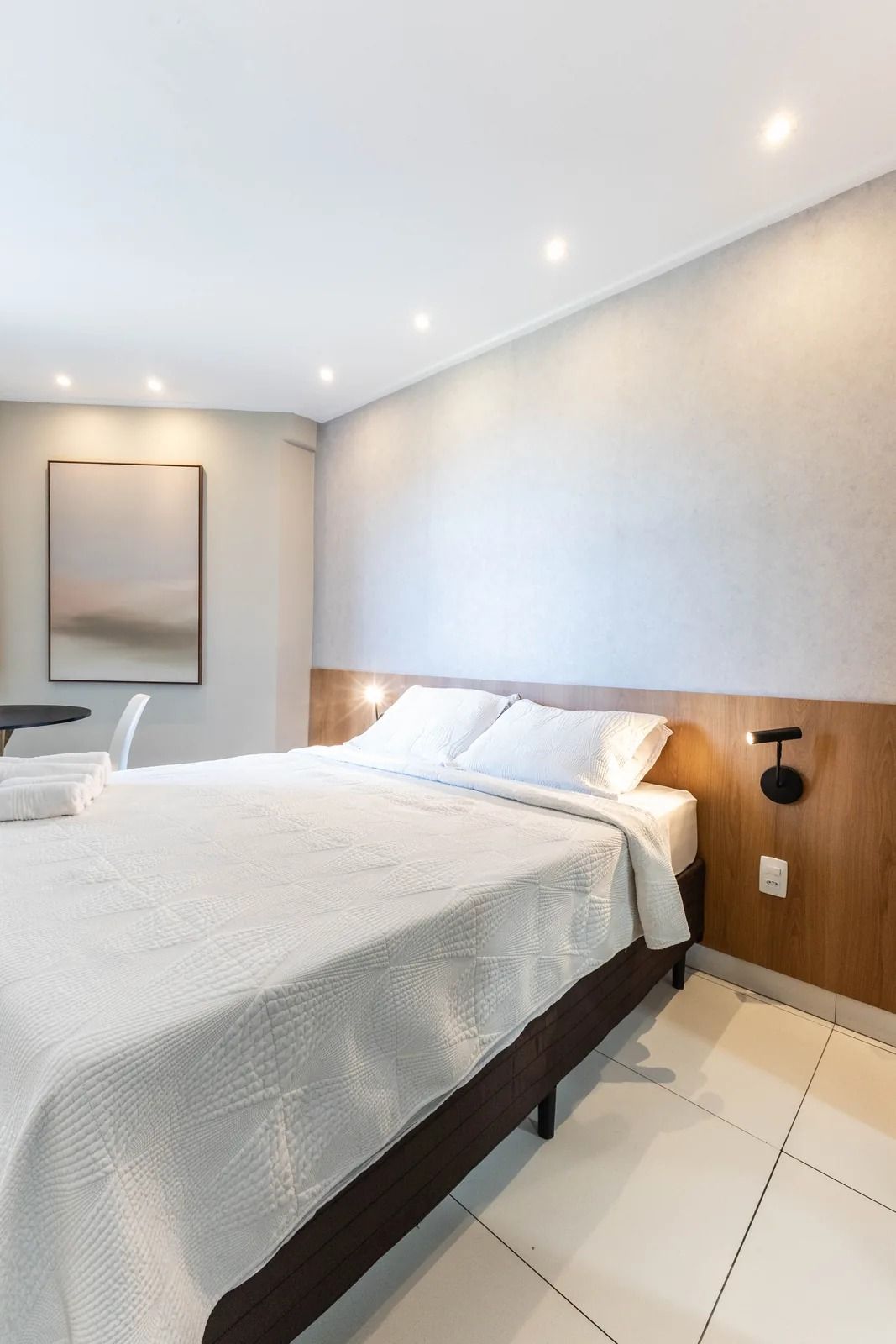 A modern hotel room with a large bed, a bedside table, and a wall-mounted light fixture.