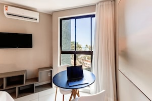 Habitación de hotel moderna con un ventanal grande, un televisor de pantalla plana en la pared, una mesa redonda con una computadora portátil y un pequeño rincón de descanso.