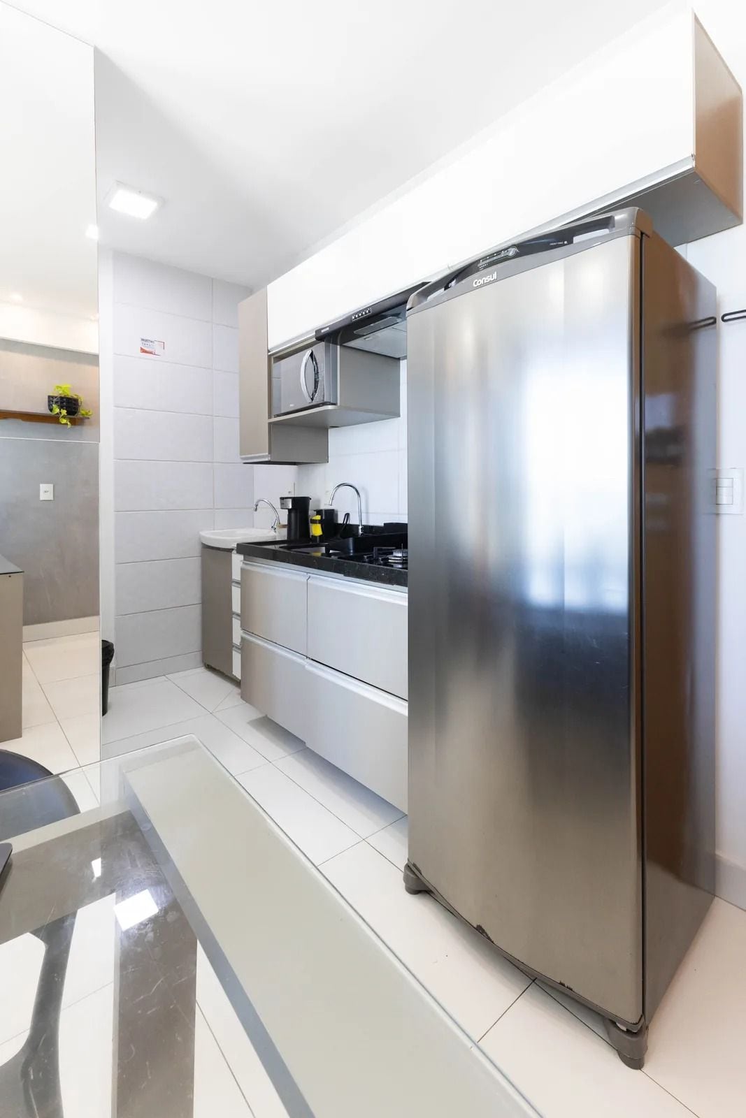 Una cocina moderna con electrodomésticos de acero inoxidable, armarios blancos y piso de baldosas.