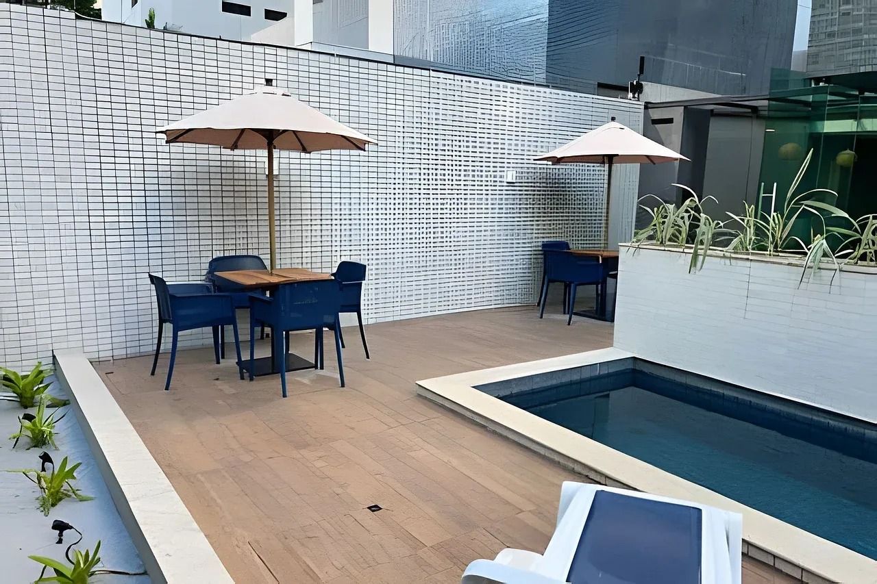 Zona junto a la piscina con mesa y sillas, sombrillas y una piscina pequeña.