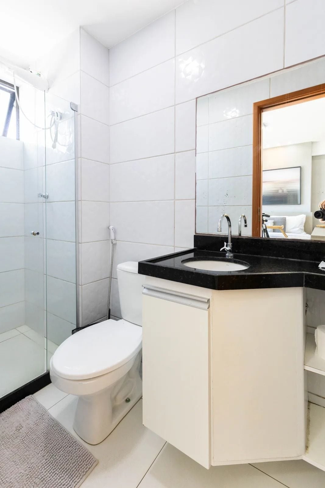 Un baño moderno con cabina de ducha de vidrio, inodoro blanco y lavamanos negro sobre encimera, con un espejo encima.