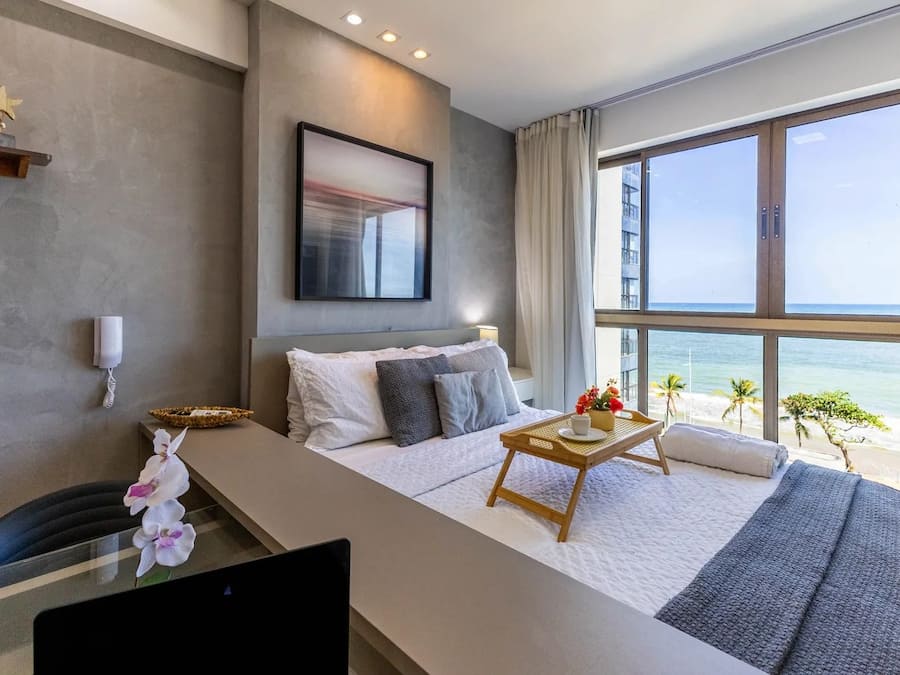 Een hotelkamer met een bed, een bureau, een groot raam met uitzicht op het strand en een schilderij aan de muur.