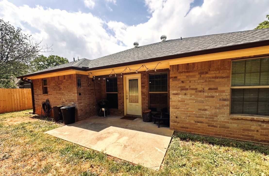 Een gelijkvloers bakstenen huis met een overdekte patio, een voordeur en een raam.