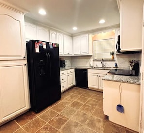 A kitchen with white cabinets, a black refrigerator, a dishwasher, and a tiled floor.