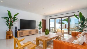 A modern living room with a flat-screen TV, wooden furniture, and a view of a pool and outdoor area. - Villa Casa Luna by Villa Plus (Playa Blanca)