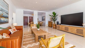 A spacious living area with a sofa, coffee table, and TV stand, featuring a large flat-screen TV and a potted plant. - Villa Casa Luna by Villa Plus (Playa Blanca)