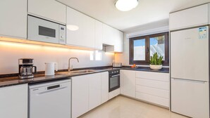 A modern kitchen with white cabinets, a built-in microwave, a coffee maker, a sink, and a refrigerator. - Villa Casa Luna by Villa Plus (Playa Blanca)